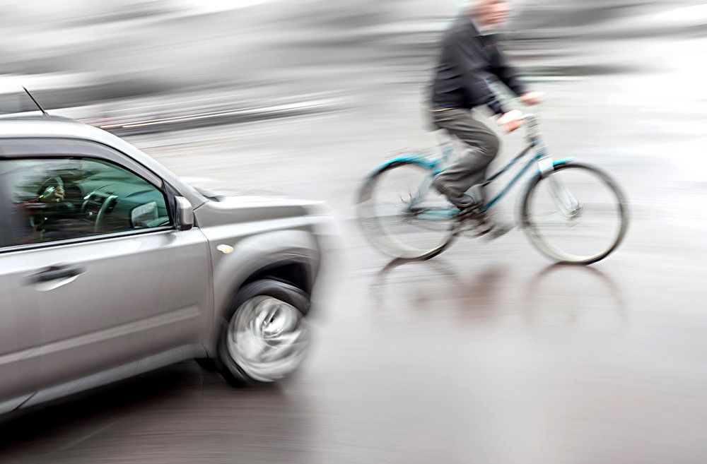 Blurry picture of man riding bike in front of car on a slick road